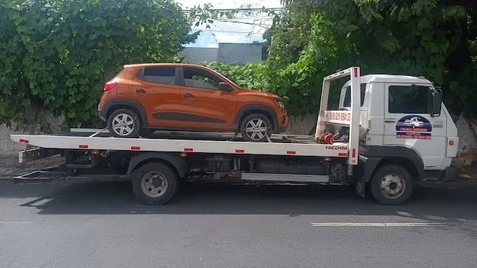 Guincho plataforma branco transportando carro compacto laranja