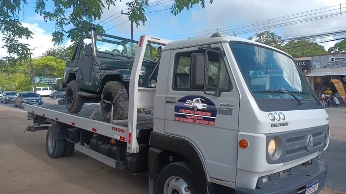 Guincho plataforma branco transportando jipe em via movimentada
