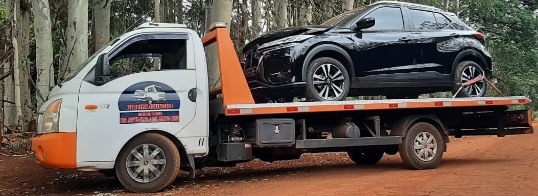Guincho plataforma transportando SUV preto em estrada de terra